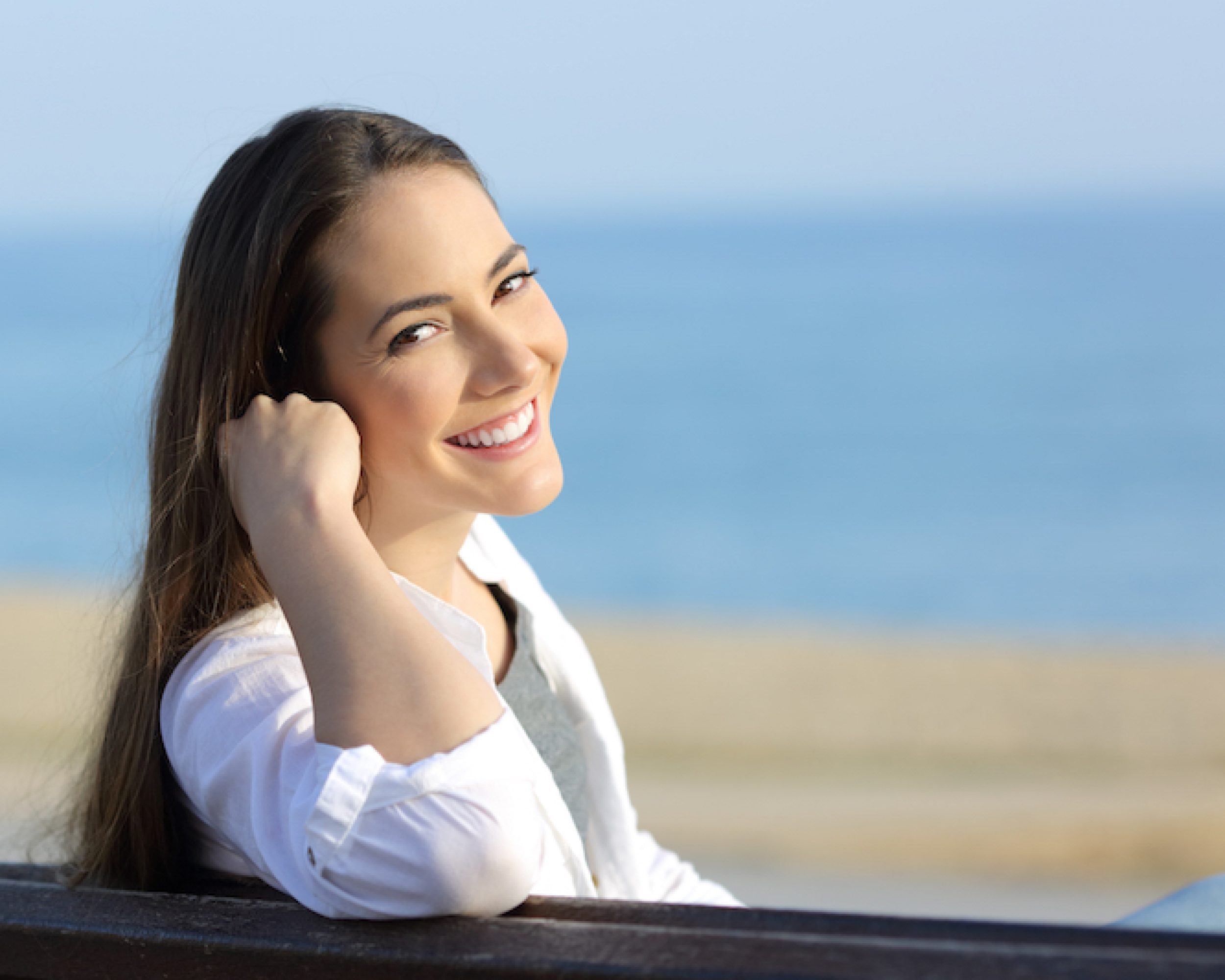 Portrait of a beauty woman smiling at camera sitting on a bench on the beach