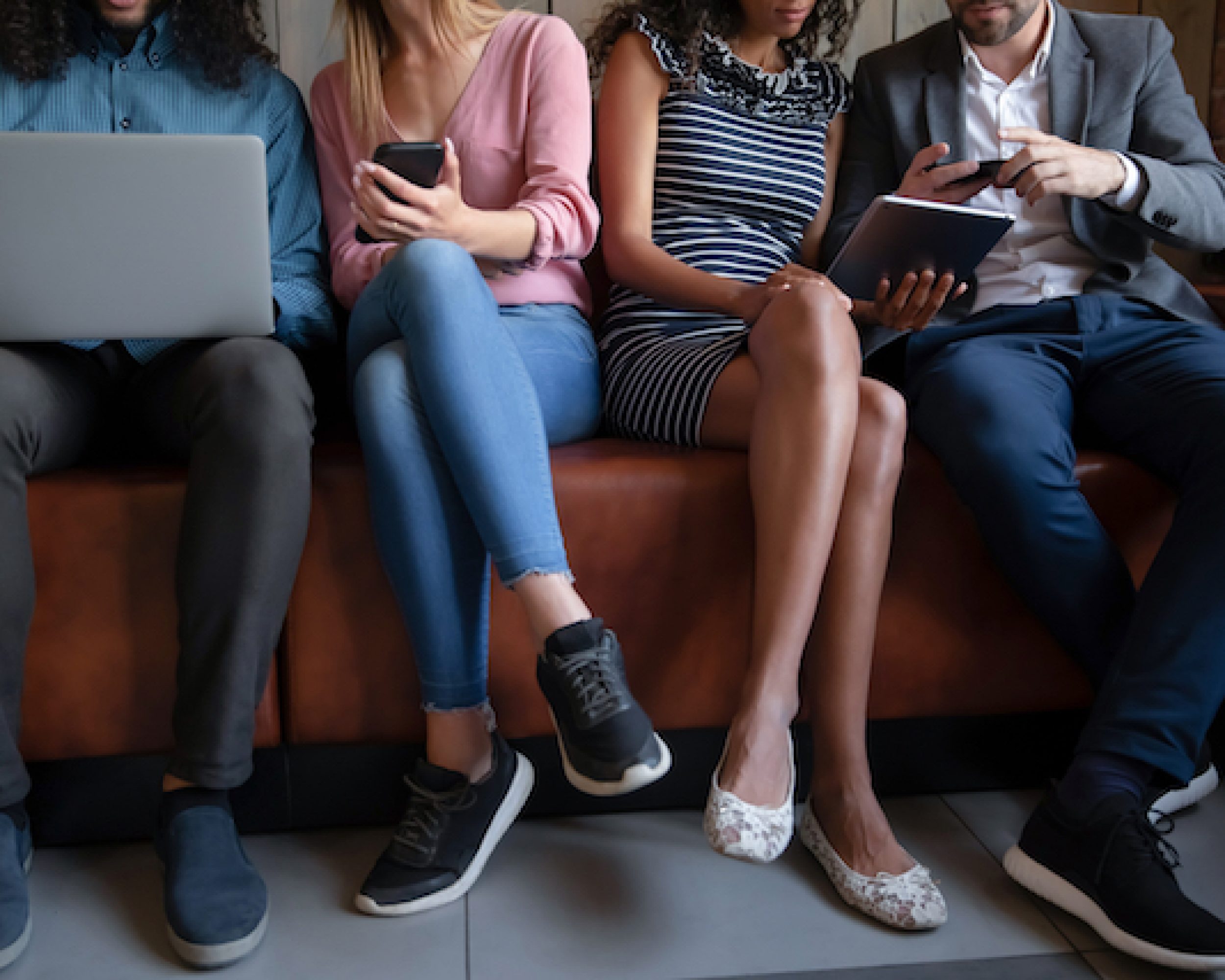 Close up cropped image diverse people using electronic devices, sitting on couch in row, young men and women chatting, looking at phones, laptop, tablet screens, gadgets addiction and overuse