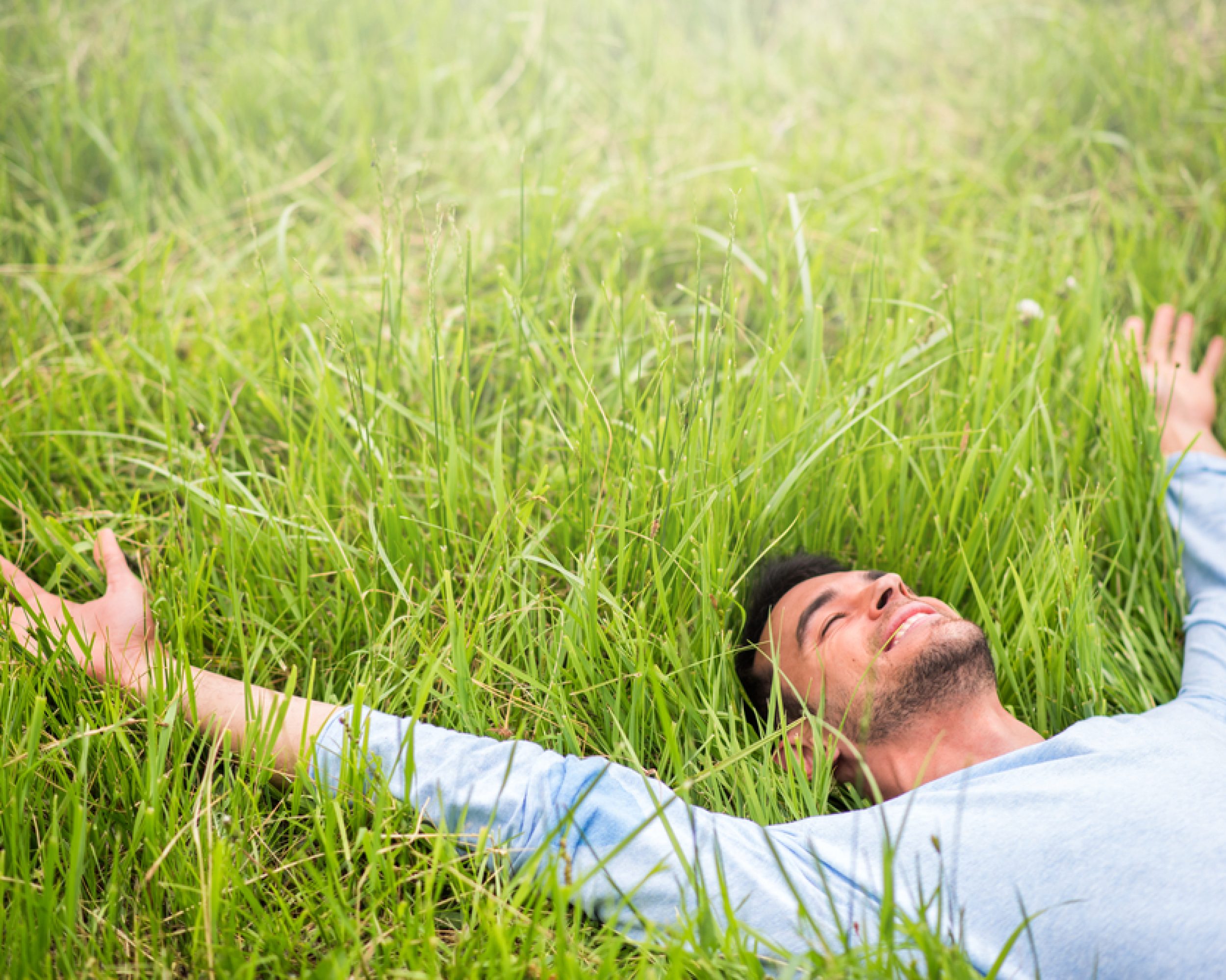 Happy,Beautiful,Man,Lying,On,The,Green,Grass,With,Arms